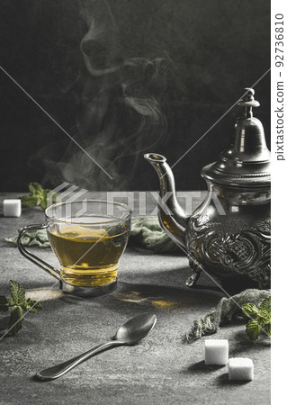 Traditional Moroccan teapot with a steaming cup of tea in a smoky black atmosphere. Vertical format. 92736810