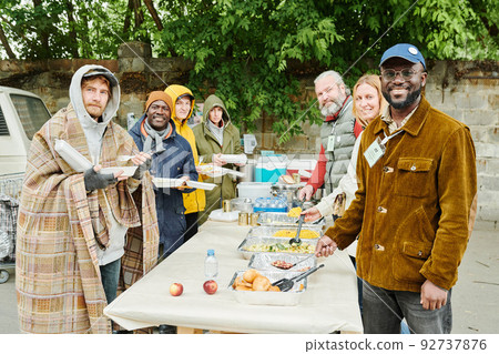 Portrait of group of volunteers and homeless people smiling at camera while arranging charity for beggars 92737876