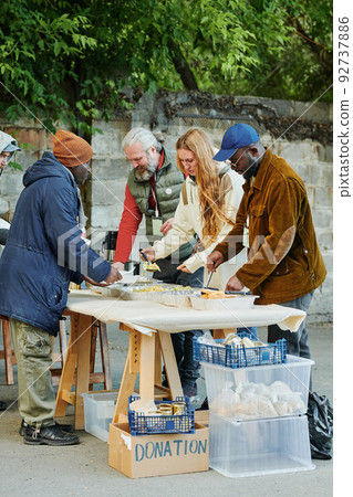 Group of volunteers serving homeless people giving them food while standing outdoors 92737886