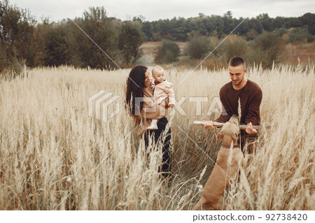 Family with cute little daughter. Father in a brown sweater. Family in a autumn field with dog Family with cute little daughter. Father in a brown sweater. Family in a autumn field with dog 92738420