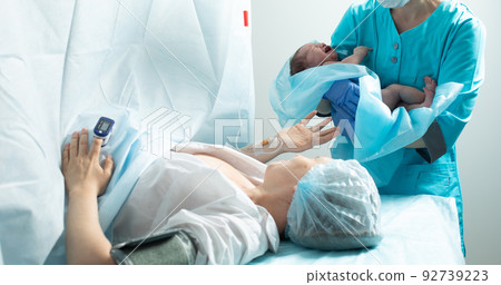 Nurse holds newborn baby close to mother in hospital 92739223