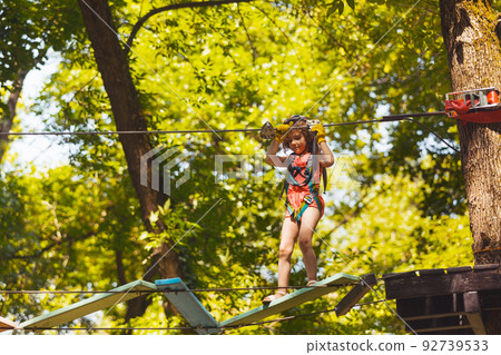 The concentrated girl carefully overcomes obstacles in the rope park The concentrated girl carefully overcomes obstacles in the rope park 92739533