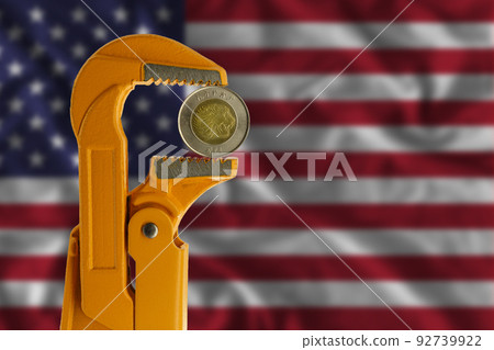 Ethiopian one Birr coin held in an orange plumber wrench on the background of the flag of the United States. Obverse of the coin. Ethiopian one Birr coin held in an orange plumber wrench on the background of the flag of the United States. Obverse of the coin. 92739922