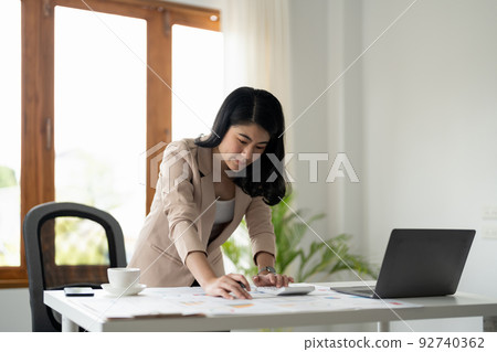 Woman with paperwork using calculator and laptop computer working at home office 92740362