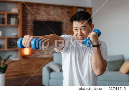 Fitness and sport concept. Active mature man exercising with two dumbbells and boxing, enjoying domestic workout Fitness and sport concept. Active mature man exercising with two dumbbells and boxing, enjoying domestic workout 92741743