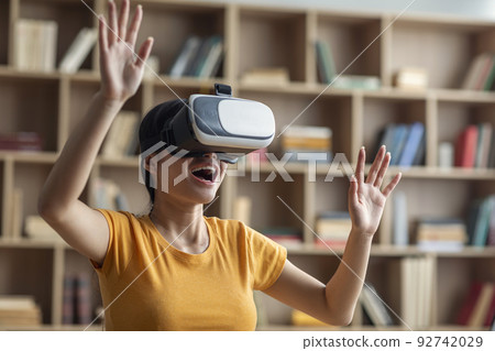 Amazed excited young asian girl in VR glasses raises hands, exploring virtual reality world at home alone Amazed excited young asian girl in VR glasses raises hands, exploring virtual reality world at home alone 92742029