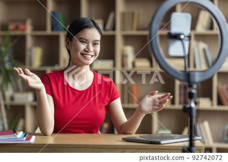 Inspired pretty smiling teen japanese lady shooting blog for student on smartphone in office interior 92742072
