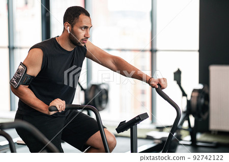Sporty Young Black Man Using Elliptical Bike Machine While Training At Gym Sporty Young Black Man Using Elliptical Bike Machine While Training At Gym 92742122