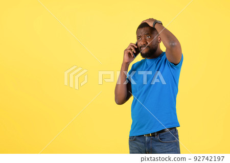 Thoughtful Black Man Talking On Cellphone Scratching Head, Yellow Background 92742197