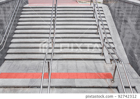 gray granite staircase with steps and stainless steel iron railings descent to the underground passage, entrance to the subway with tactile red tiles and a ramp for the disabled, top view, nobody. gray granite staircase with steps and stainless steel iron railings descent to the underground passage, entrance to the subway with tactile red tiles and a ramp for the disabled, top view, nobody. 92742312