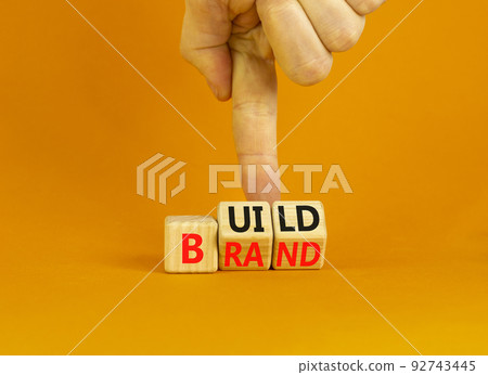 Build your brand symbol. Concept words Build brand on wooden cubes. Businessman hand. Beautiful orange table orange background. Build your brand and business concept. Copy space. 92743445