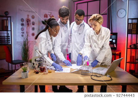 Diverse team of multiethnic scientists standing near table with research results Diverse team of multiethnic scientists standing near table with research results 92744443