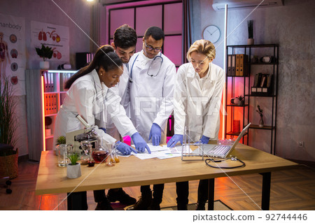Diverse team of multiethnic scientists standing near table with research results Diverse team of multiethnic scientists standing near table with research results 92744446