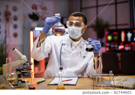 Experienced male scientist in protective mask and goggles doing analysis of substance. Experienced male scientist in protective mask and goggles doing analysis of substance. 92744601