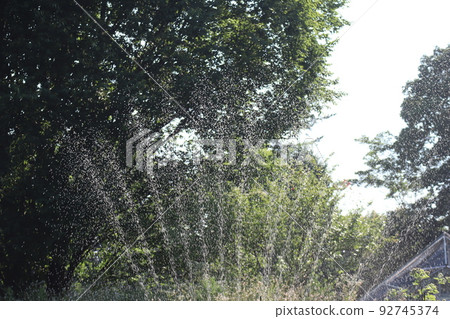 Scenery with a sprinkler that sprinkles water with green trees in the background 92745374