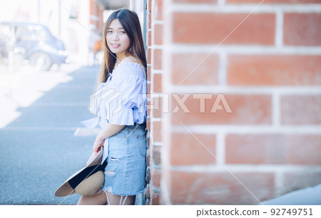 Portrait of young asian woman leaning on the brick wall and looking at camera. 92749751
