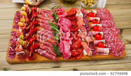 Slicing sausages fuet, ham, salami, chorizo with cherry tomatoes and olives Slicing sausages fuet, ham, salami, chorizo with cherry tomatoes and olives 92749896