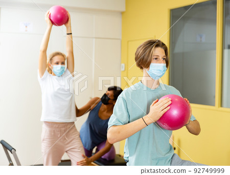 Teenagers in masks training pilates in gym with trainer Teenagers in masks training pilates in gym with trainer 92749999