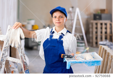 Portrait of female professional painter in blue overall with paint roller Portrait of female professional painter in blue overall with paint roller 92750088