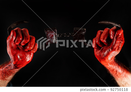 A man with bloody hands holds iron handcuffs. 92750118