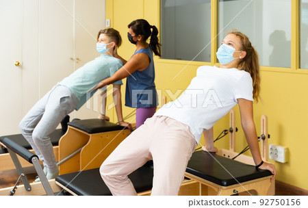 Teenagers in masks training pilates in gym with traine Teenagers in masks training pilates in gym with traine 92750156