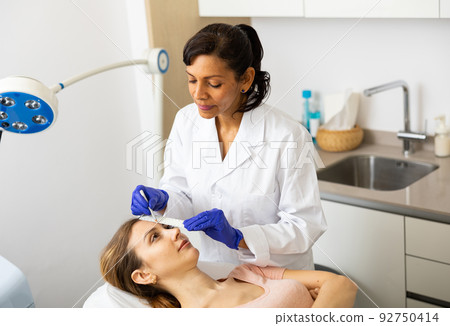 Female cosmetologist marking skin of young woman with white pencil 92750414