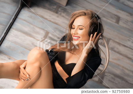 Photo of a happily smiling young woman in headphones. She sits in the morning in a rotational chair and listens to music. 92750980