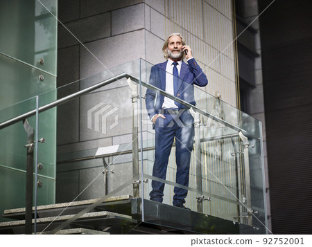 mature caucasian businessman making a call using mobile phone inside modern office building mature caucasian businessman making a call using mobile phone inside modern office building 92752001