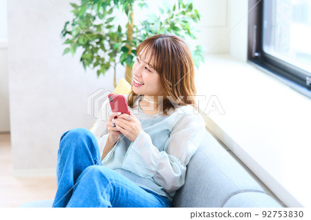 Young woman in plain clothes, living room, smartphone Young woman in plain clothes, living room, smartphone 92753830