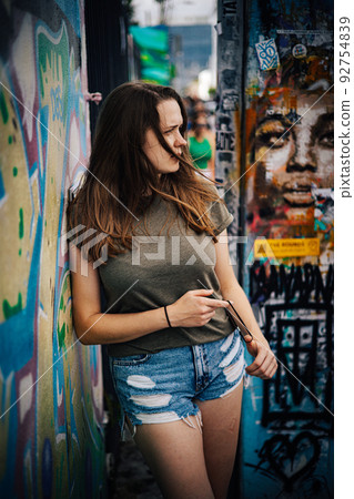 Young and beautiful woman leans against a colorful wall and poses for the camera - typical street 92754839