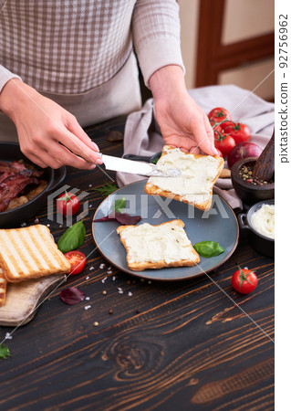 making bacon and cheese sandwich - woman smearing cream cheese on toasted bread making bacon and cheese sandwich - woman smearing cream cheese on toasted bread 92756962