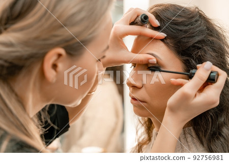 Make-up artist makes a professional make-up of a young woman in the studio. 92756981