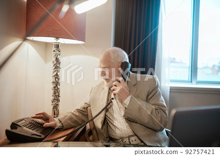 A gray-haired gentleman calling to the room service A gray-haired gentleman calling to the room service 92757421