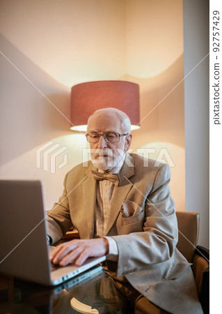 Senior man sitting at the laptop and looking busy 92757429