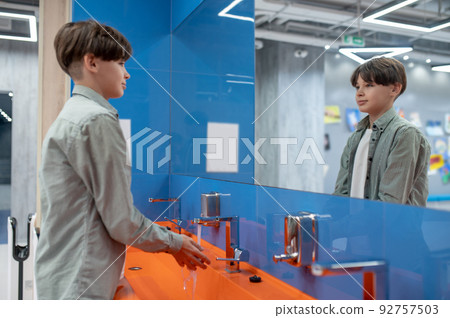 A boy washing hands in a school toilet 92757503