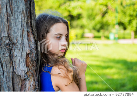 Girl long curly hair lean on tree trunk, lonely child 92757894