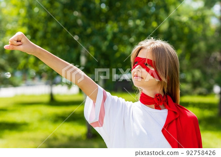 Funny teenager girl playing power super hero over green park background Funny teenager girl playing power super hero over green park background 92758426