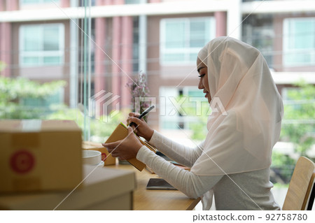 Muslim female online store small business owner seller entrepreneur packing package post shipping box preparing delivery parcel on table. Ecommerce dropshipping shipment service concept. 92758780