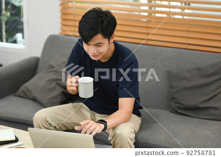 Asian man in casual clothes drinking coffee and surfing internet or checking email on laptop at home 92758781
