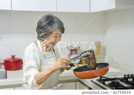 Senior woman grilling steak Senior woman grilling steak 92758919