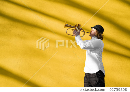 Young caucasian long-haired man in shirt and hat playing trumpet outdoors Young caucasian long-haired man in shirt and hat playing trumpet outdoors 92759808
