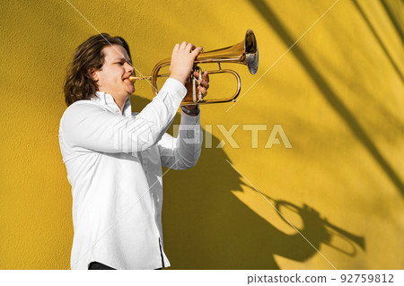 Young caucasian long-haired man in shirt playing trumpet outside on festival Young caucasian long-haired man in shirt playing trumpet outside on festival 92759812