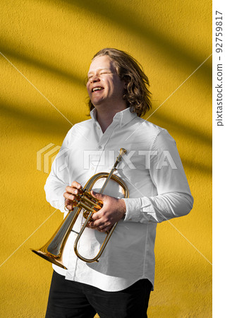 Young European male well-dressed cheerful smiling jazzman with trumpet outside Young European male well-dressed cheerful smiling jazzman with trumpet outside 92759817