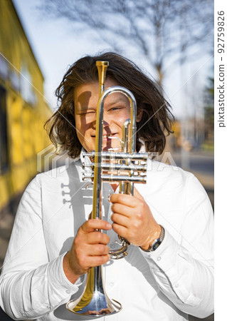 Young caucasian male cheerful jazzman looking through trumpet on sunny street Young caucasian male cheerful jazzman looking through trumpet on sunny street 92759826