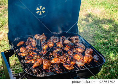 Spicy chicken legs and wings grilling in a portable barbecue. Spicy chicken legs and wings grilling in a portable barbecue. 92761702