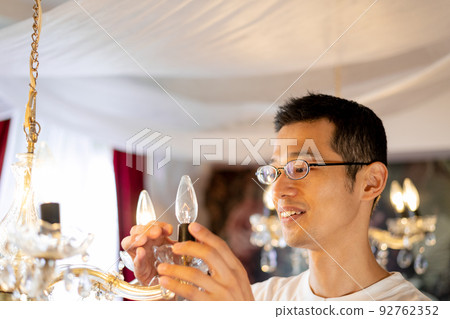 A man changing a light bulb in a chandelier 92762352