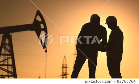 oil production. two silhouette workers work as a team next to an oil pump. business oil production production concept. two engineers of the oil and sun gas industry are discussing a business plan oil production. two silhouette workers work as a team next to an oil pump. business oil production production concept. two engineers of the oil and sun gas industry are discussing a business plan 92763764