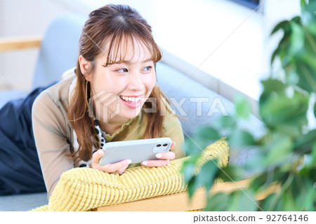 Young woman in plain clothes, living room, smartphone Young woman in plain clothes, living room, smartphone 92764146