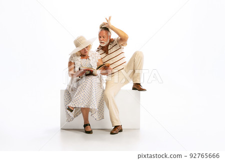 Emotional senior man and woman in her 60's in vintage attire sitting together isolated on white background. Concept of relationship psychology, age, fashion Emotional senior man and woman in her 60's in vintage attire sitting together isolated on white background. Concept of relationship psychology, age, fashion 92765666