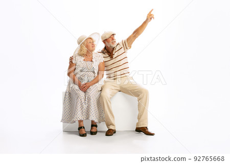Emotional senior man and woman in her 60's in vintage attire sitting together isolated on white background. Concept of relationship psychology, age, fashion 92765668